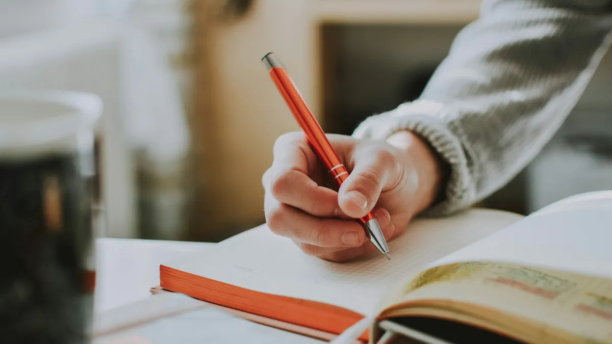 Hand writing in an open journal with an orange pen