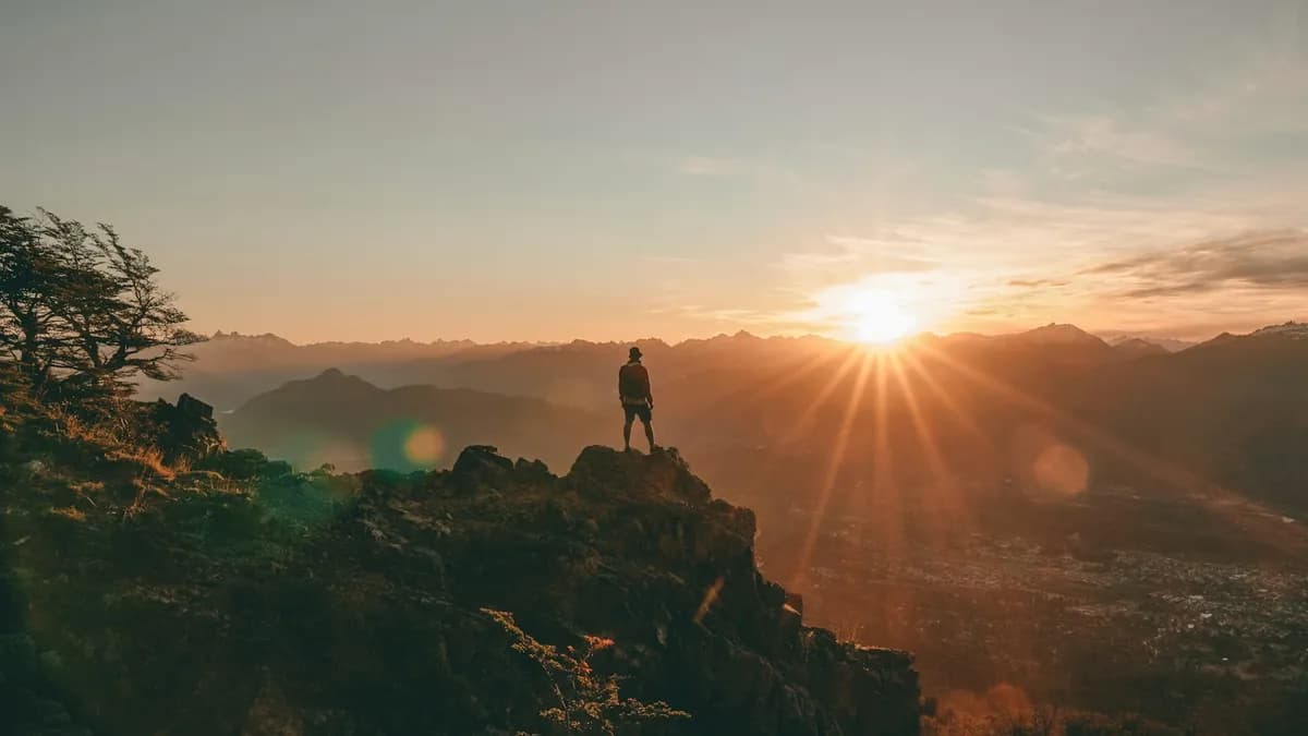 Person standing on a rocky summit watching the sun rise over a mountain valley