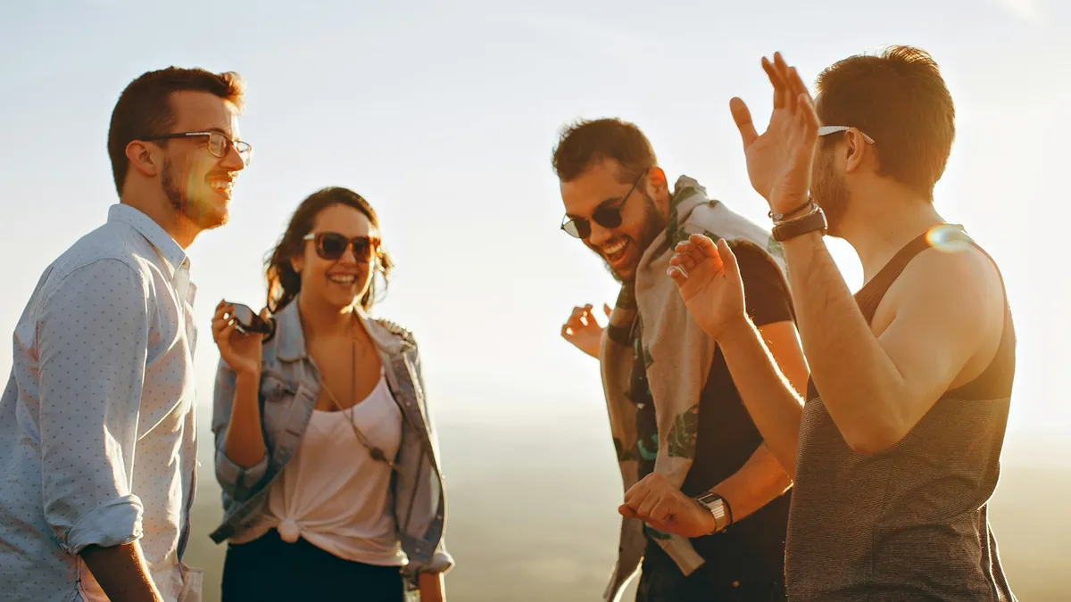 Four friends laughing together outdoors in warm sunlight